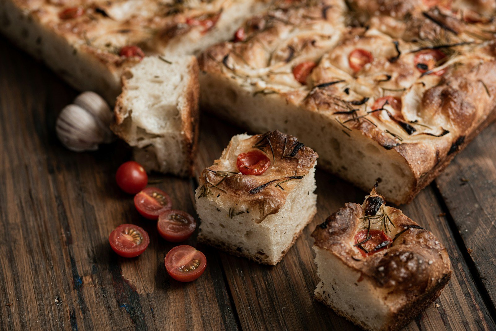 Focaccia coupée en parts, romarin et tomates cerises, prête à servir