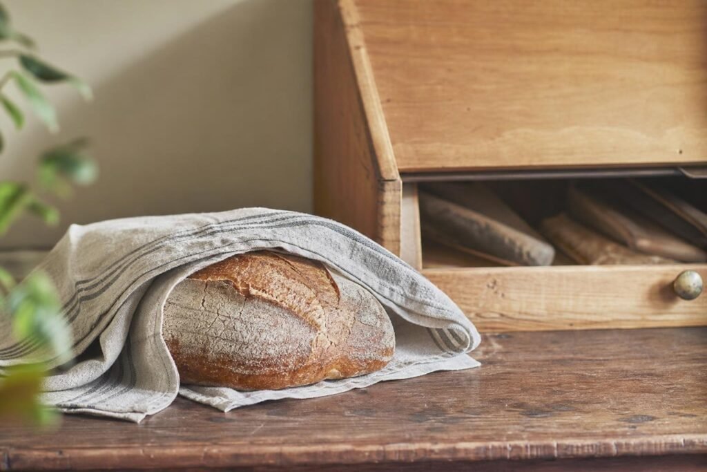 Miche de pain enveloppée dans un torchon en lin, posée à côté d'une huche à pain en bois