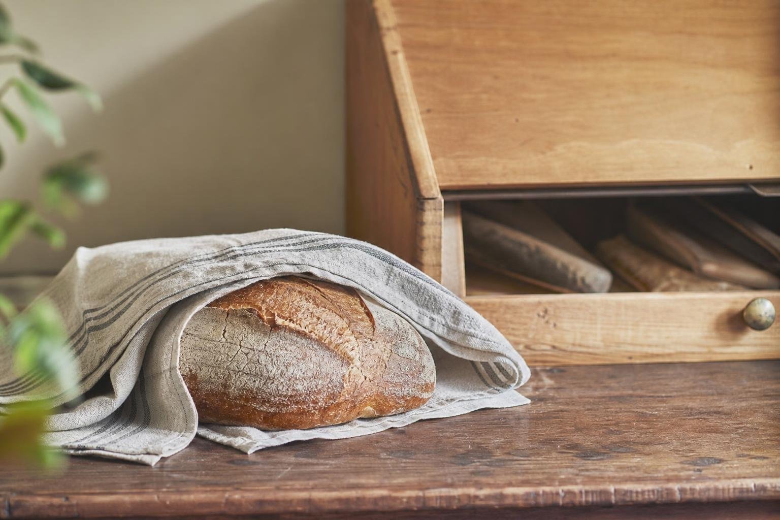 Miche de pain enveloppée dans un torchon en lin, posée à côté d'une huche à pain en bois