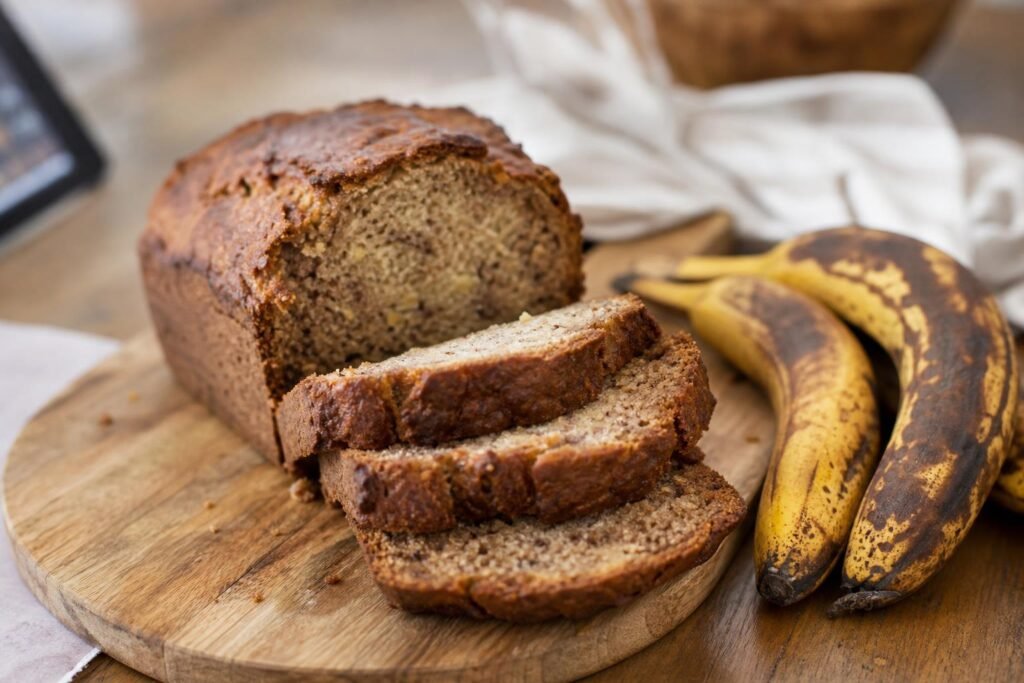 Banana bread tranché sur une planche, à côté de bananes très mûres